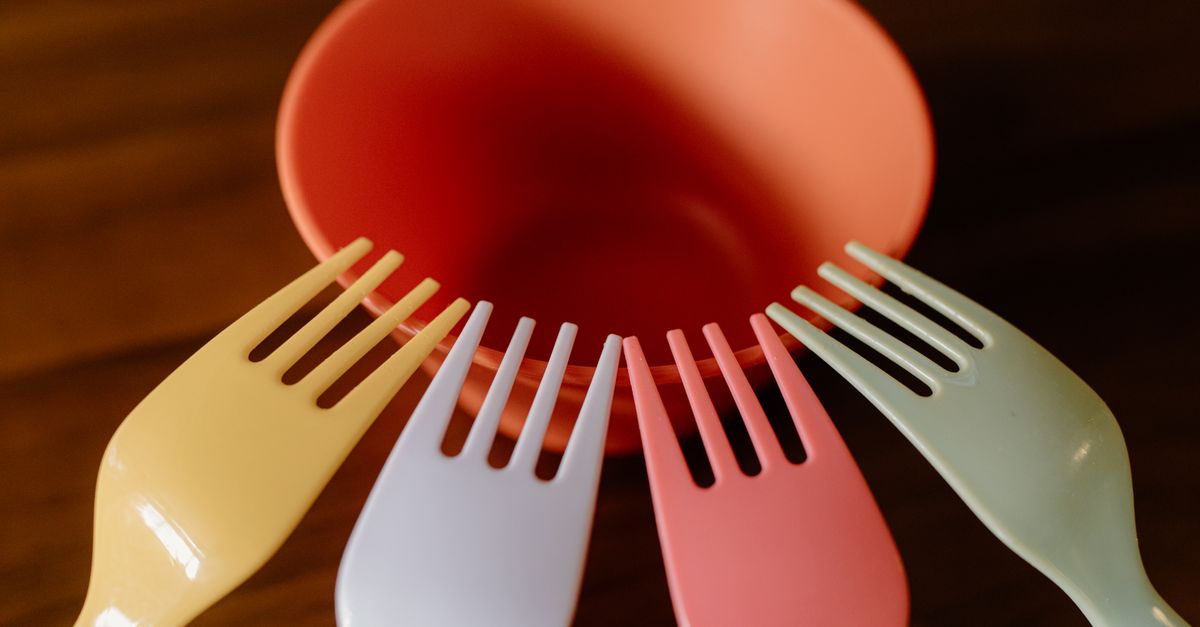 A vibrant close-up of colorful plastic forks surrounding an orange bowl on a wooden table.